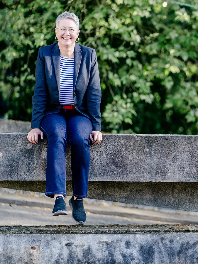 Susanne Jestel sitzt lachend auf einer Betonbrüstung und lässt die Beine baumeln als Symboldbild für die Zusammenarbeit mit ihr unter ihrem Motto "Marketing einfach machen".