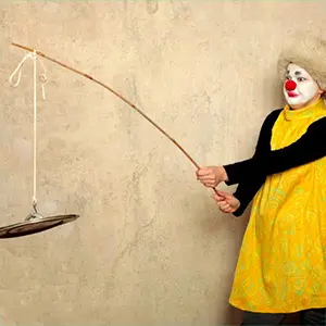 Sirkka Remes im Clownskostüm mit roter Nase und einem gelben Kleid angelt mit einem Topdeckel begleitend zu ihrem Kompliment zur Zusammenarbeit mit Susanne Jestel.