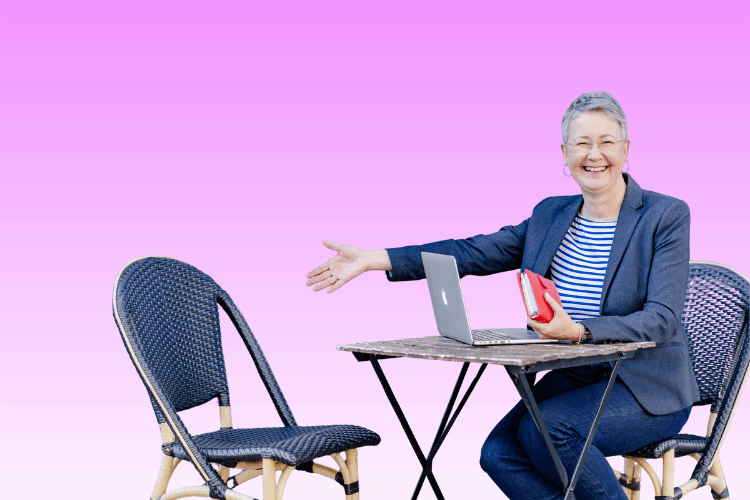 Susanne sitzt am Tisch und macht einladende Handbewegung